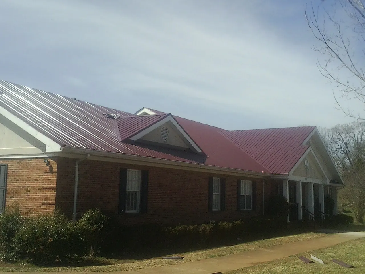 Red metal roof with gabled entries on a long brick building, from a Hail Damage Roof Repair job in Alvada
