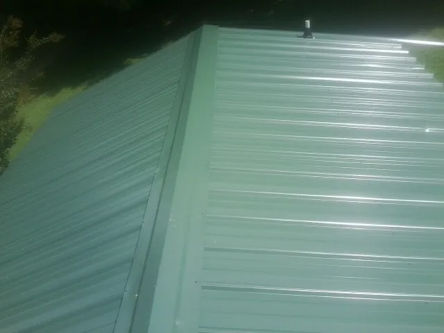 New green metal panels meeting at the ridge of a roof — Flat Roof Repair work by our crew in Alvada
