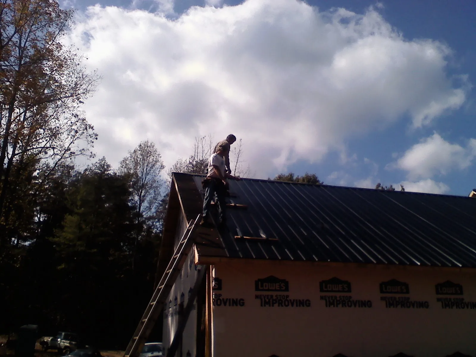 Roofer fastening dark metal panels high against a cloudy sky, from a Roof Inspection job in Alvada