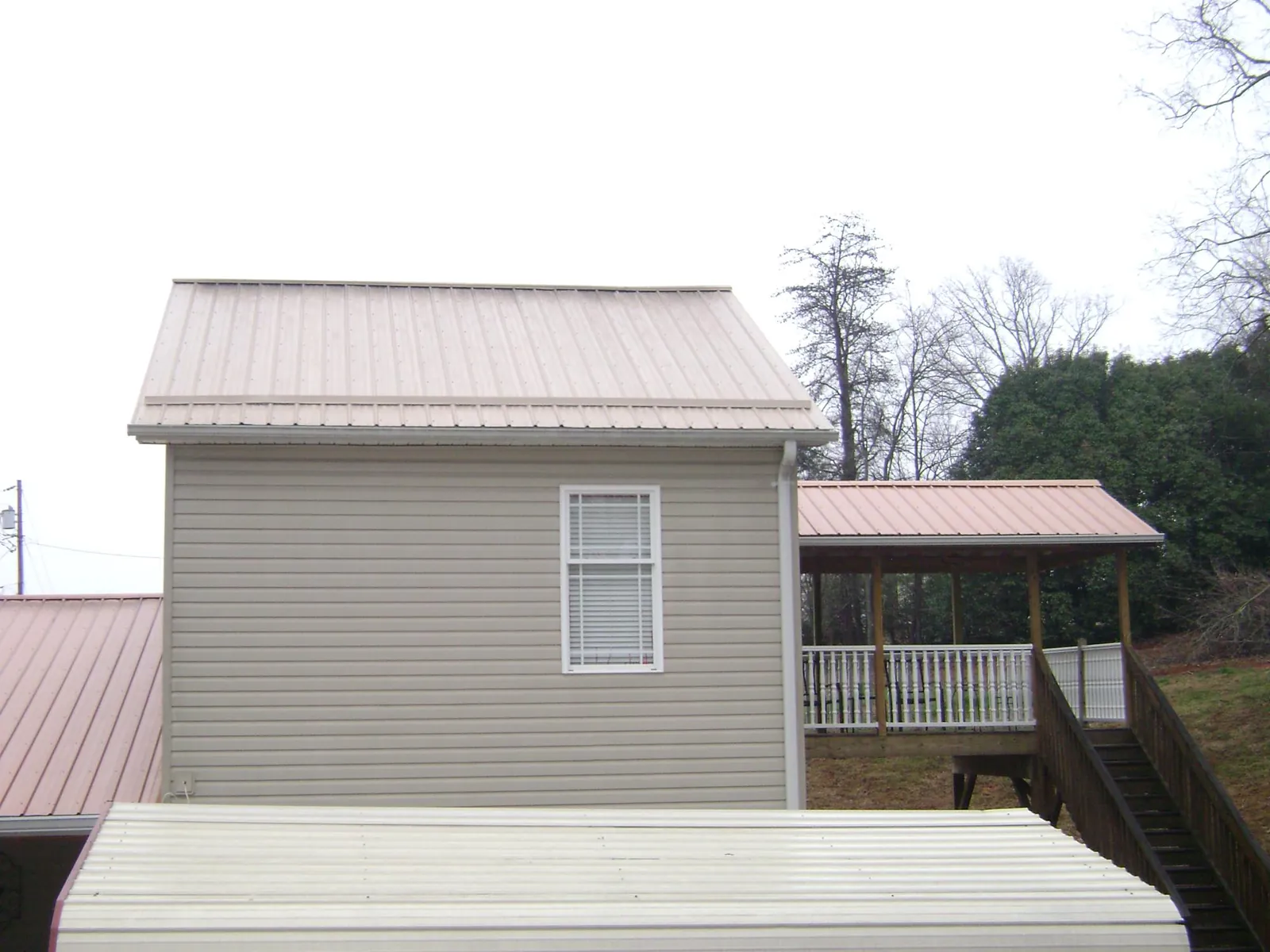 Tan metal roofs on a two story addition and attached porch, from a Roof Replacement job in Alvada